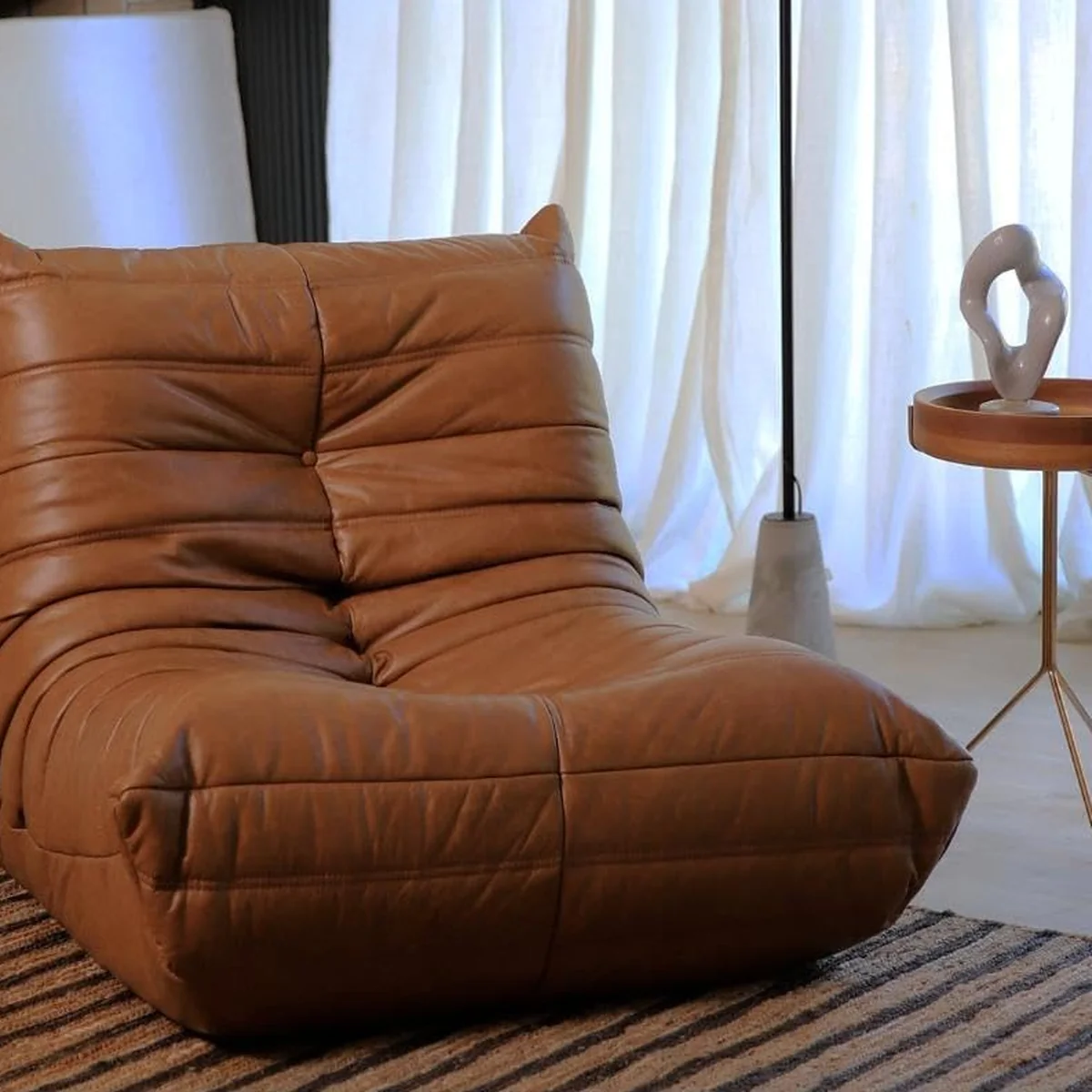 Poltrona Nirvana em couro caramelo com design estilo togo, silhueta baixa e acolchoada, ideal para ambientes modernos e despojados