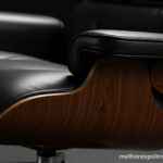 Close-up nos detalhes de uma Poltrona Charles Eames, mostrando a junção da madeira laminada com o couro, símbolo de design e luxo.